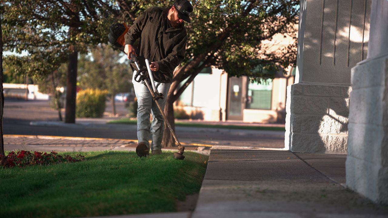Crew member trimming the lawn edge along a sidewalk at a commercial building