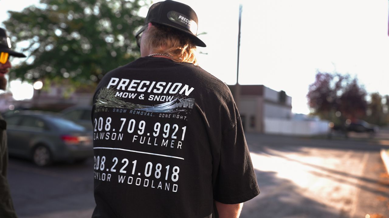 Back of a black crew shirt printed with Precision Mow and Snow, Mowing. Snow Removal. Done Right., and both owner phone numbers