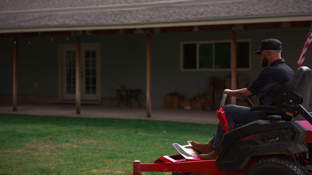 Crew member mowing the front lawn of a home on a red zero-turn mower at sunset